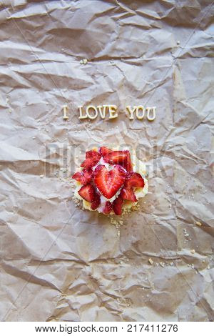 Bright cupcake with strawberries lies on craft paper, the inscription I love you.