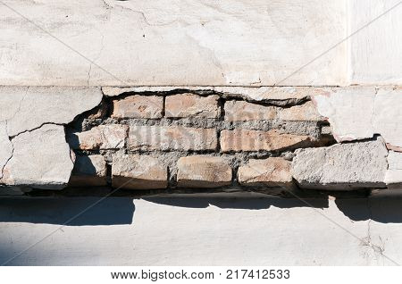 Bad foundation base on old house or building cracked plaster facade wall with brick background