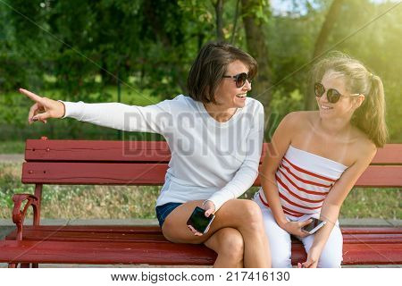 Communication between parent and child. Mom and daughter teenager talking and laughing while sitting on the bench in the park