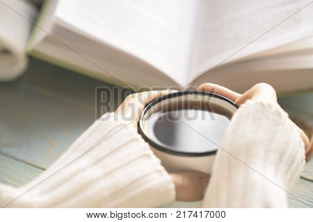 Girl reads book and drinks tea on window sill during winter holidays. Cosy home atmosphere. Hygge and leisure concept