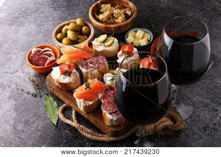 Italian antipasti wine snacks set. Cheese variety Mediterranean olives pickles salami salmon tomatoes artichokes and wine in glasses. Spanish tapas