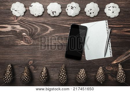 Brown wood background. Gold cones and sweet biscuits arranged diametrically opposed. Letter and phone, space for a greeting message. Top View. With Christmas.