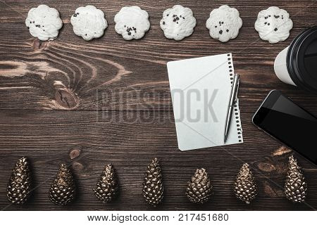 Brown wood background. Gold cones and sweet biscuits arranged diametrically opposed. Letter, telephone and coffee, space for a greeting message. Top View.