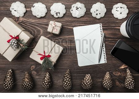 Brown wood background. Gold cones and sweet biscuits arranged diametrically opposed. Letter, phone, star, coffee and gifts, space for a greeting message. Top View.