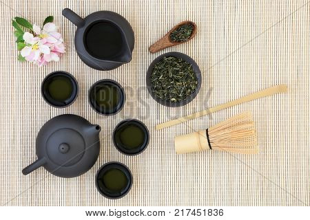 Sencha sukiygu makoto Japanese tea with teapot and cups, dried leaves, whisk, stick stirrer and spring blossom on bamboo background.
