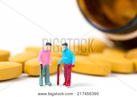 Miniature People, Small Figure Old Man Or Patient Holding Walking Stick With Vitamin C Pill Or Table