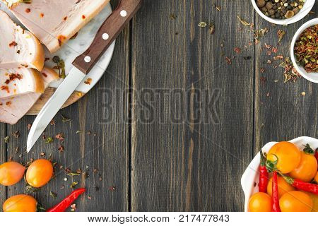 A smoked brisket sliced with a knife and yellow cherry tomatoes on a dark wooden rustic background top view