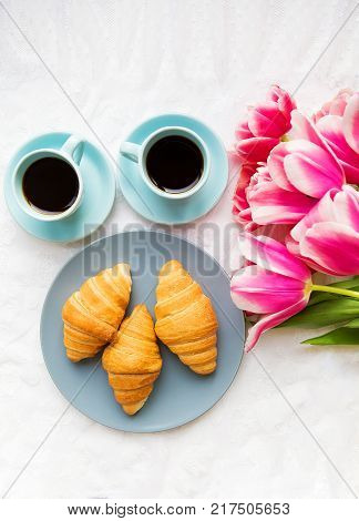 two cups of coffee, croissants and a bouquet of pink tulips, beautiful morning.