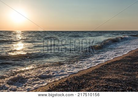 Sea waves at sunset at the shore with seashells. Beautiful background.