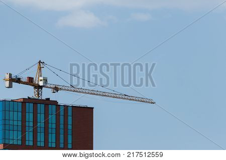 The roof of a new city high-rise building and the boom of a construction crane in the sky.