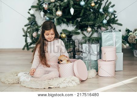 The girl sits at the tree and looks at the gifts. New Year holidays. The time to realize dreams. A gift in the box. New Year's Symbol