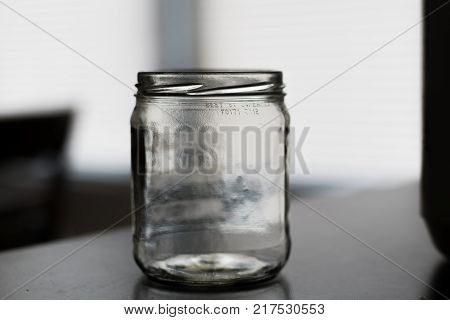 Empty mason jar without lid on a kitchen table with window in the background