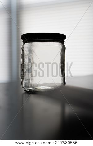 Empty mason jar with lid on a kitchen table with window in the background
