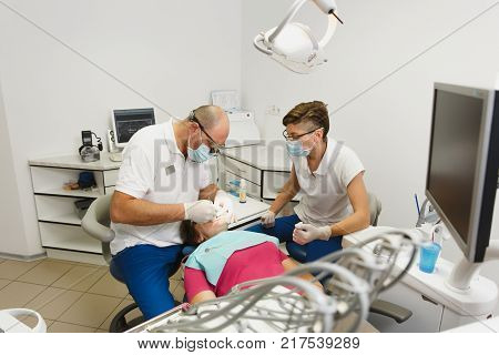 Process Of Preparing And Installing Dental Ceramic Crown. Male Professional Dentist And Female Assis