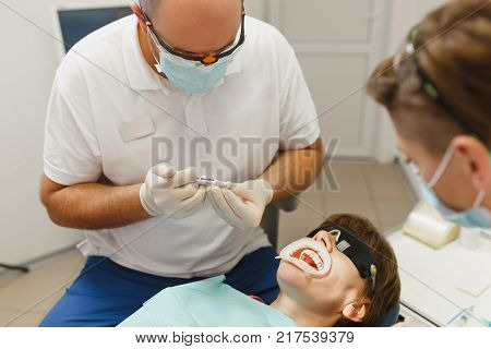 Process Of Preparing And Installing Dental Ceramic Crown. Male Professional Dentist And Female Assis