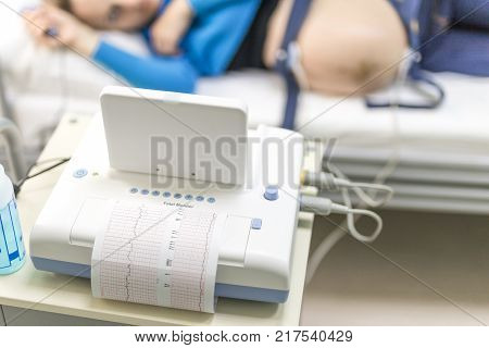 Young happy woman lying on a bed in a hospital while doctor setting a cardiotocography sensor to examine  fetus heartbeat.