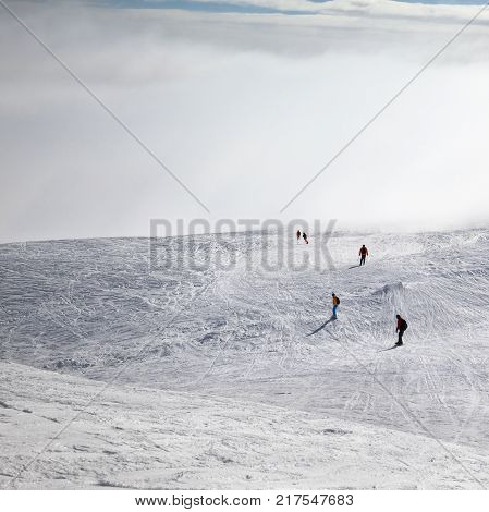 Skiers and snowboarders downhill on snowy and sunlight sky in haze at cold winter morning. Caucasus Mountains Georgia region Gudauri.