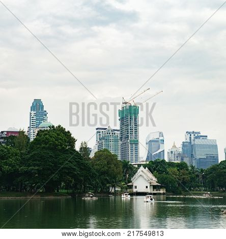 Bangkok, Thailand - December 23, 2015: People relax on boat in a city park. Pleasureboats on a lake in the heart of Bangkok - Lumphini Park. Business district cityscape with cloudy sky in the evening