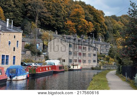 hebden bridge with barges and houseboats on the rochdale canal with old stone houses and surrounding woodland in autumn
