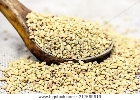 Fenugreek Seeds In A Wooden Scoop On A Gunny Background.