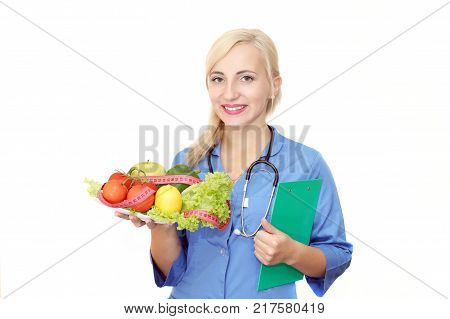 A smiling female doctor a nutritionist holds in his hand a plate of useful and fresh vegetables and fruits. Healthy eating.