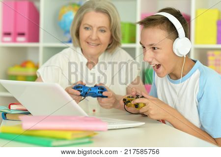 Happy granny with her grandson playing computer game with laptop at home