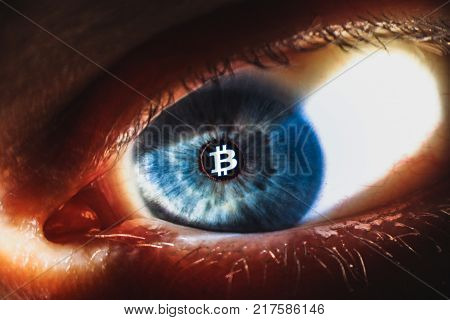 An enlarged image of eye with a blue iris, eyelashes and sclera. Bitcoin symbol inside the pupil. the shot is made by a slit lamp with integrated camera. Cryptocurrency concept.