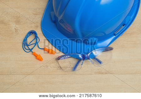 A hard hat safety glasses and a pair of ear plugs isolated on a wooden background