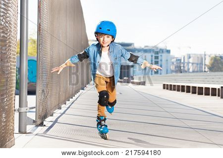 Portrait of preteen boy in helmet practicing rollerskating with his hands like wings at outdoor rollerdrome