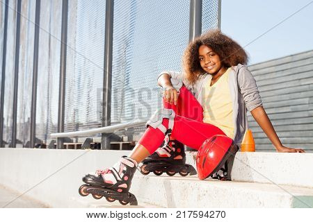 Happy African girl sitting on the stairs in roller skates at rollerdrom