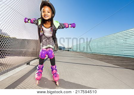 Preteen African girl in roller blades and protective gear doing tricks at skate park