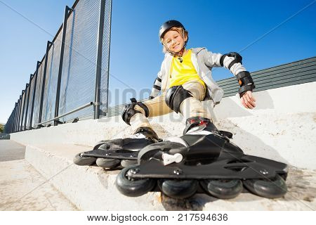 Happy blond boy sitting on the stairs in roller skates at rollerdrom
