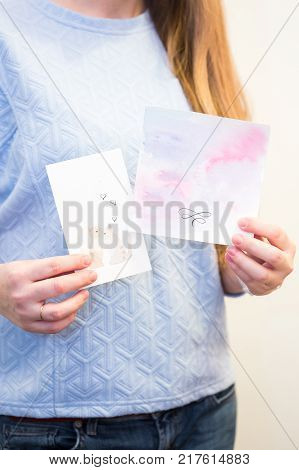 crafting, holidays, birthday party concept. there is redhaired woman wearing blue sweatshirt, she is holding in her arms two not sighned greeting cards that are handmaden