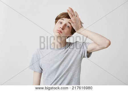 Tired fair-haired young man feels headahce after hard work, touches head with hand, stressed. Regretful caucasian guy has forgetful expression, tries to remember all necessary details