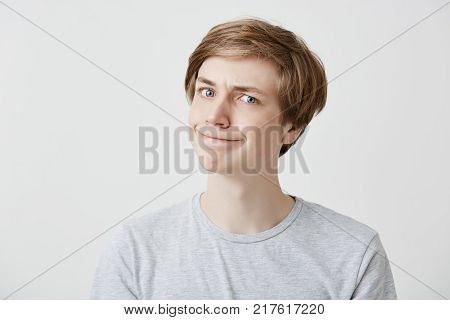 Portrait of fair-haired young man curves lips, looks in bewilderment, puzzled, his faces expresses misunderstandment, receives bad news. Shocked male has troubles at home or at university. People and reaction concept