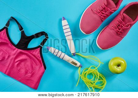 Flat lay of female sport equipments in pink color with jump rope and sneakers on blue background. Sports and healthy lifestyle concept. Top view. Copy space. Still life