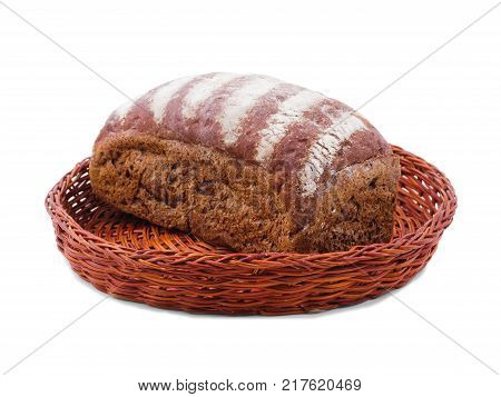 In a wicker brown basket there is a freshly baked loaf of black bread sprinkled with flour on top. Isolated on white background.
