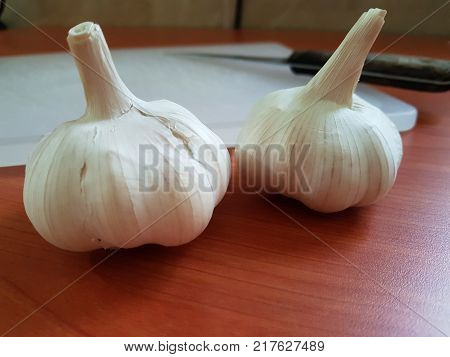 Still life close-up image of garlic bulbs on table with blur background of knife and cutting board