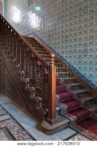 Cairo Egypt - December 2 2017: Wooden staircase with ornate red carpet decorated wooden balustrade and Turkish ceramic tiles wall at the Residence hall Manial Palace of Prince Mohammed Ali