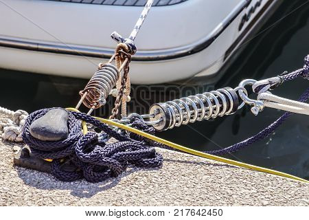Metal cleat for mooring boats, bolted to the ground, with rope and shock absorber spring .