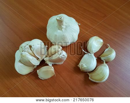 High angle still life image of white garlic in unpeeled 
whole bulb head, cluster and clove form on wooden table