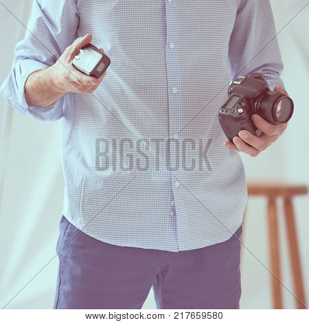 Closeup of young man holding digital camera with synchronizer in studio, focus is on synchronizer, image with vintage toning