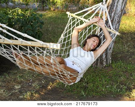 beautiful young brunette woman lies in a hammock enjoying rest and relaxation. sexy woman dressed in a white jersey and shorts. top view