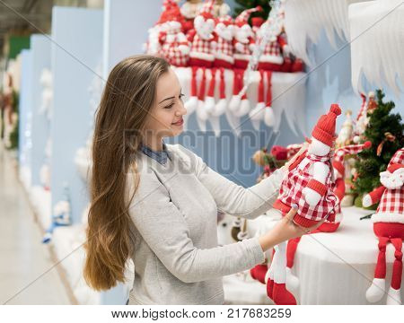 Cheerful happy customer girl choosing gifts for Christmas and New Year. She is holding snowman toys in big supermarket
