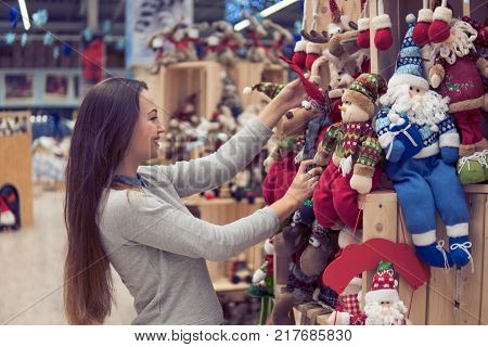 Cheerful happy customer girl choosing gifts for Christmas and New Year. She is holding New Year's deer and Santa Claus toys