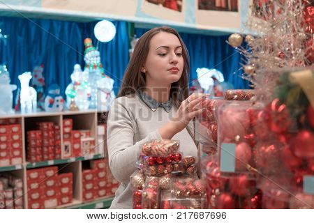 customer girl choosing red Christmas tree decoration balls. difficult decision. Various choice
