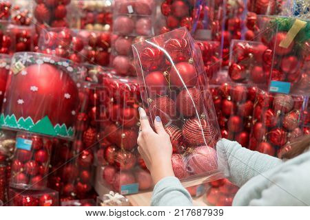 closeup view of customer girl hands taking red Christmas tree decoration balls. difficult decision. Various choice