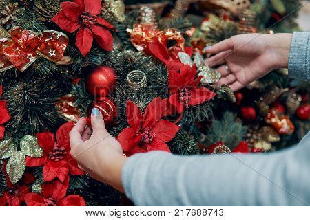 Closeup view of hands decorating Christmas tree with decoration balls. Beautiful holiday decoration.