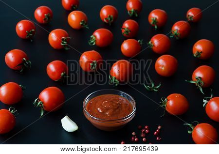 Juicy ripe tomatoe and and tomato sauce or ketchup in glass bowl on black background. Selective focus.