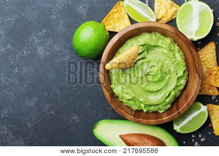 Fresh guacamole dip with avocado lime and nachos on black table top view. Copy space.Traditional mexican food.